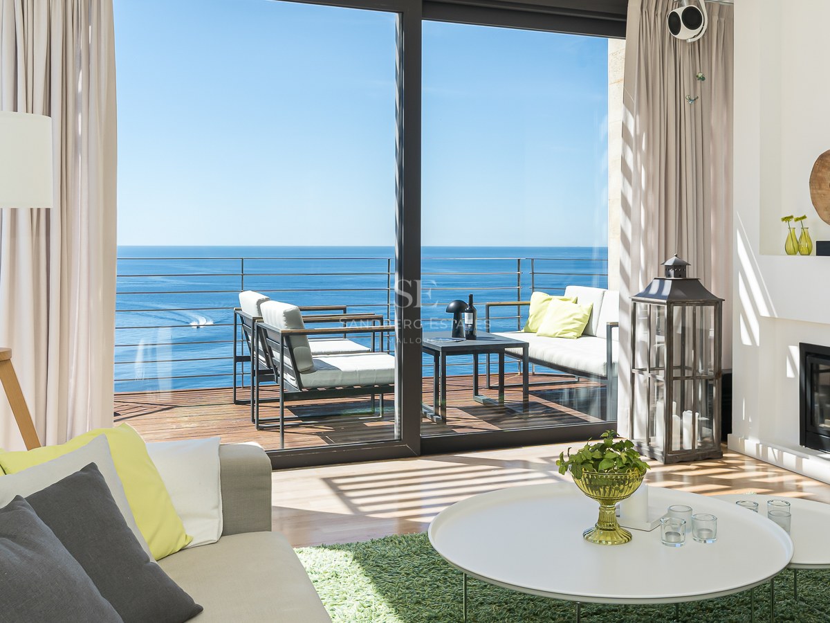 Salon moderne avec cheminée et baies vitrées ouvrant sur une terrasse avec vue directe sur la mer Méditerranée.