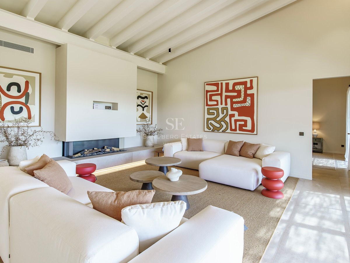 Helles Wohnzimmer mit hohen Balkendecken, modernem Kamin, weißen Sofas und abstrakter Wandkunst.