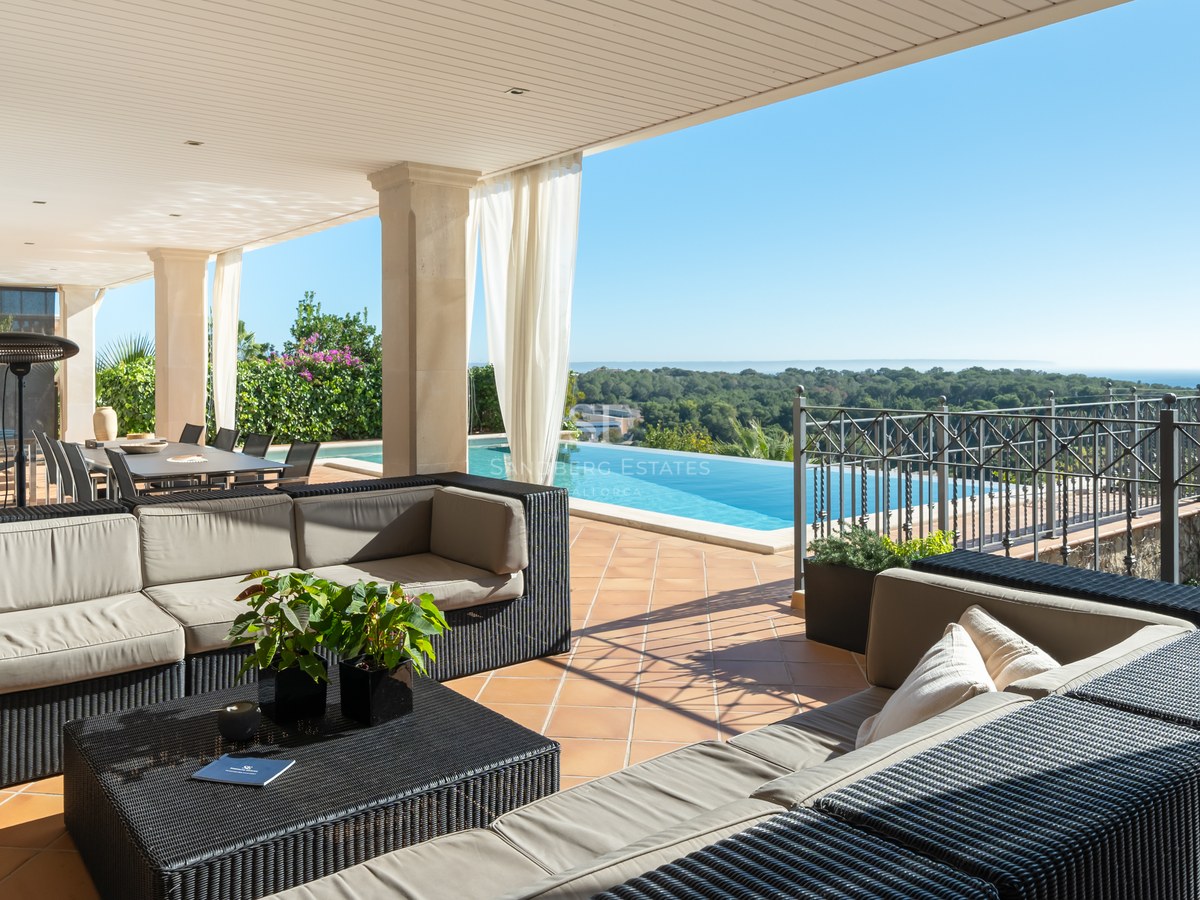 Terrasse de luxe ombragée avec canapés en osier, sol en terre cuite et piscine à débordement sur la mer.