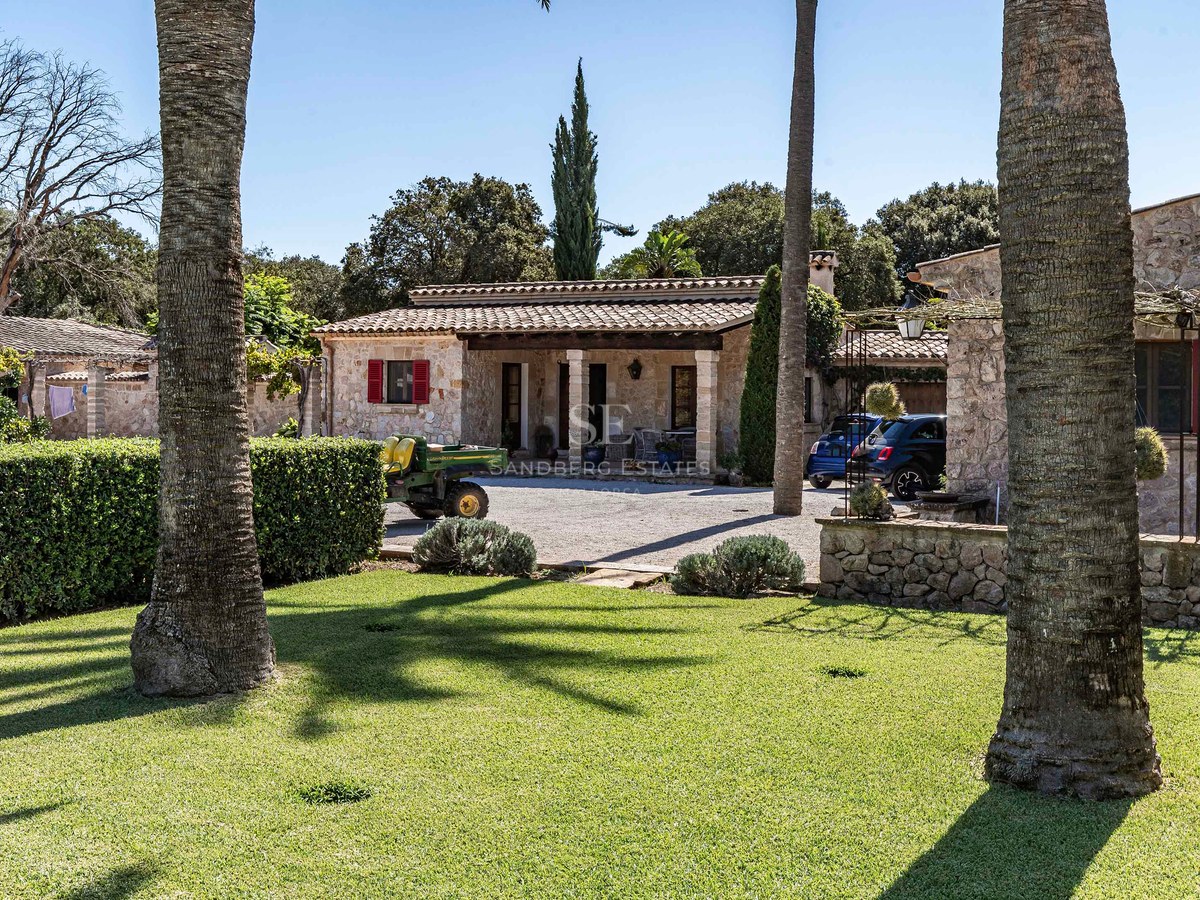 Villa rustique en pierre avec volets rouges et toit en tuiles, entourée d'une pelouse verdoyante et de palmiers.
