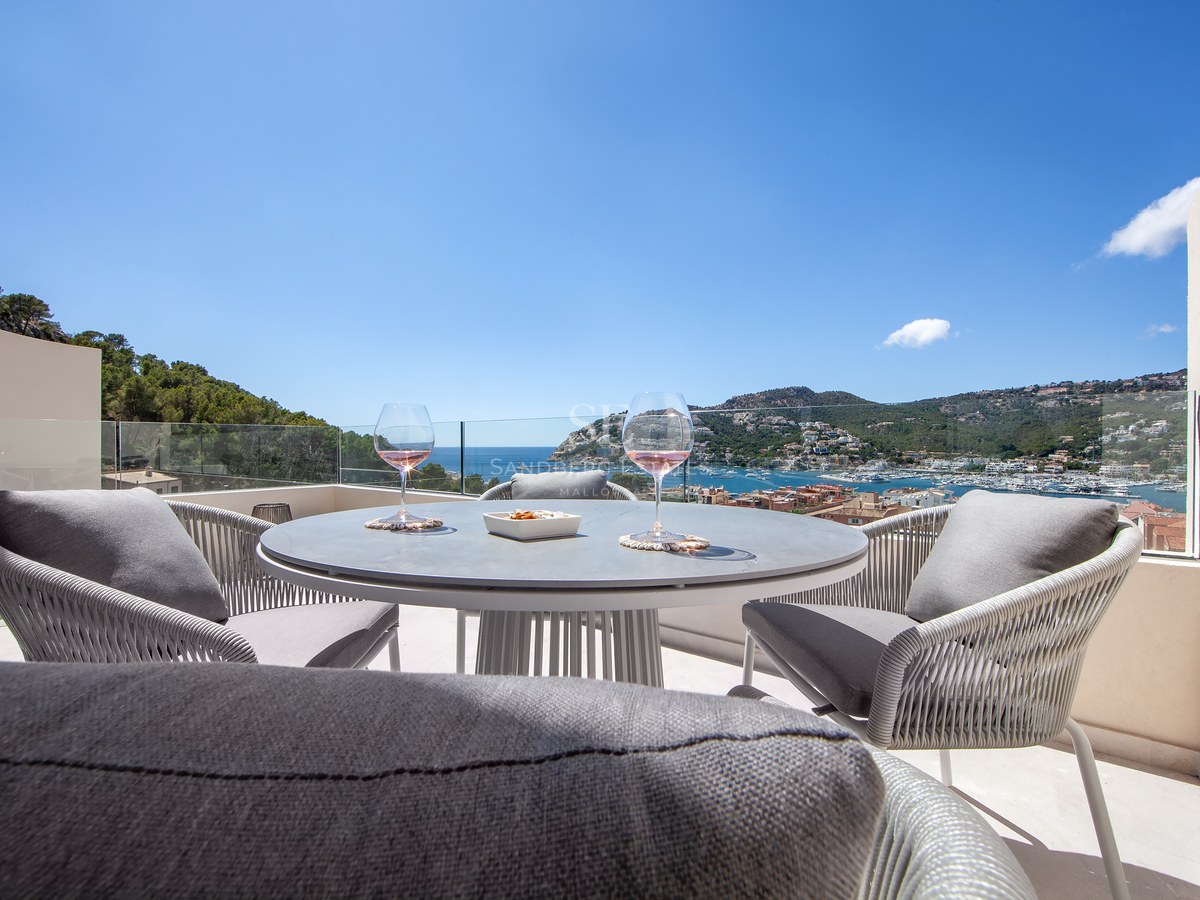 Modern terrace table with two glasses of wine set against a spectacular view of the harbor and sea under a clear blue sky.