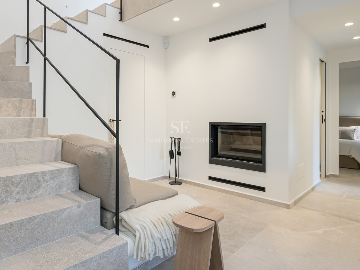 Intérieur moderne avec escalier en pierre claire, rampe noire minimaliste et cheminée murale intégrée.