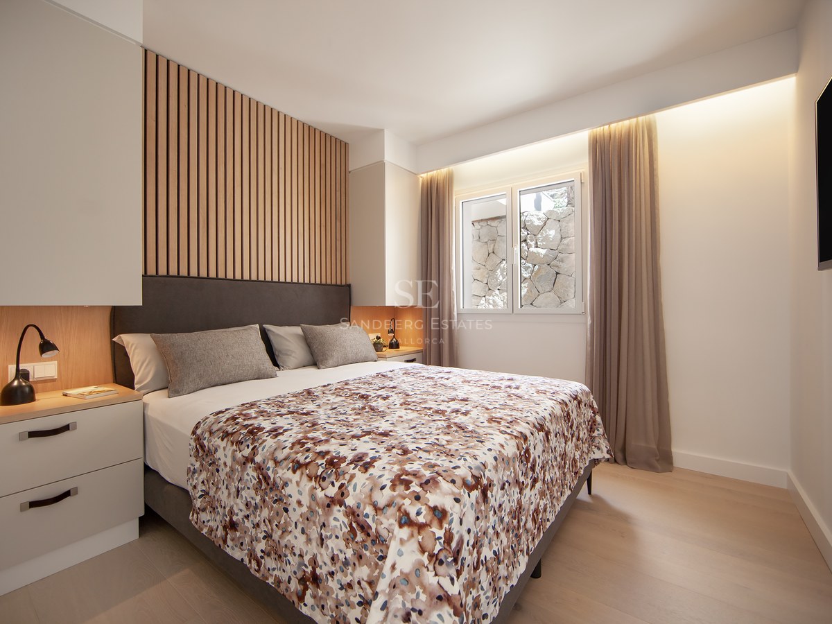 Modern master bedroom featuring a grey bed, wood slat headboard detail, warm bedside lighting, and a window.