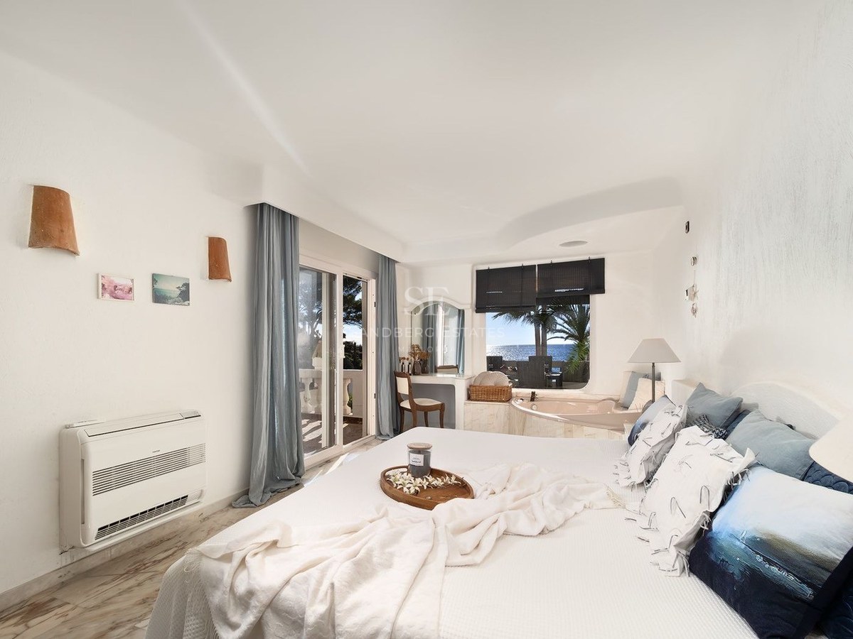 Chambre principale blanche et lumineuse avec baignoire intégrée près de la fenêtre et balcon vue mer.