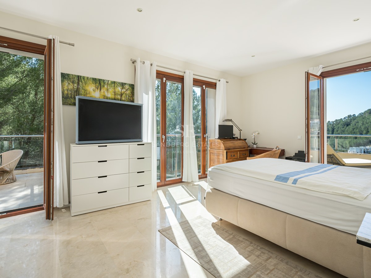 Dormitorio luminoso con suelo de mármol, cama doble y puertas de cristal a una terraza con vistas al monte.