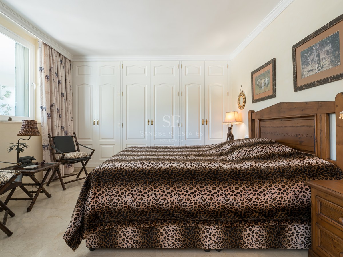 Bedroom featuring leopard print bedding, dark wood furniture, and a full wall of white built-in wardrobes.