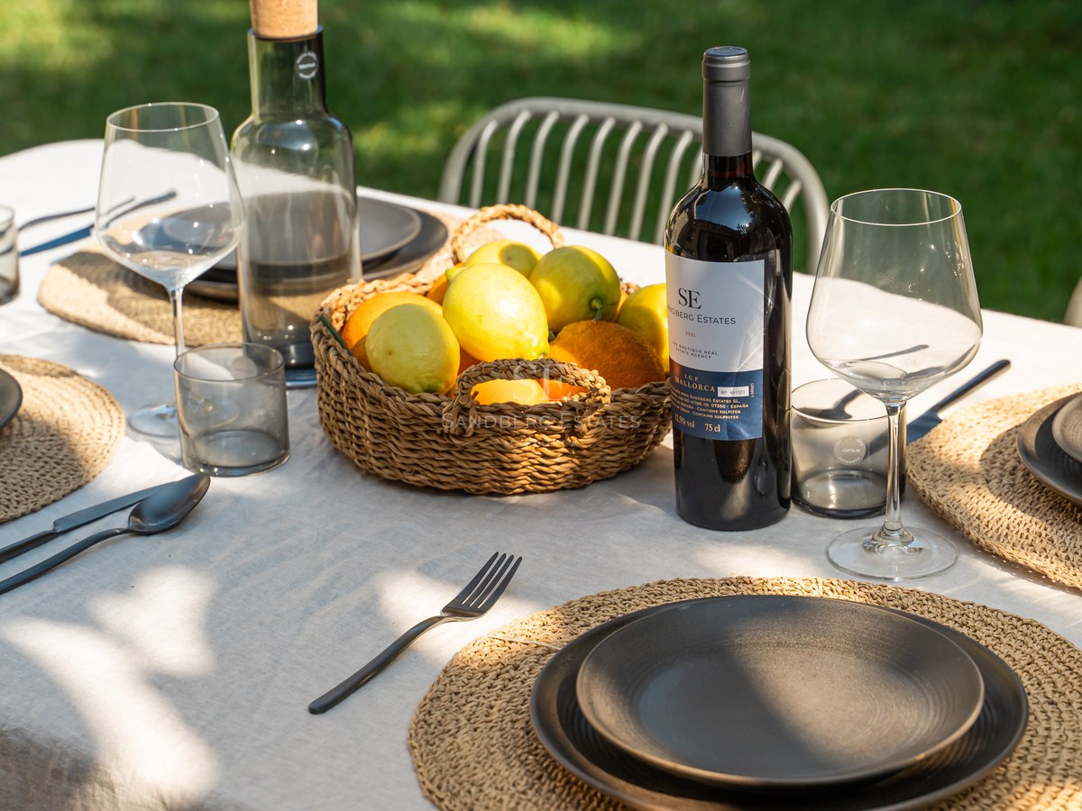 Table de salle à manger extérieure dressée avec du lin, de la vaisselle noire, du vin de Majorque et des citrons.