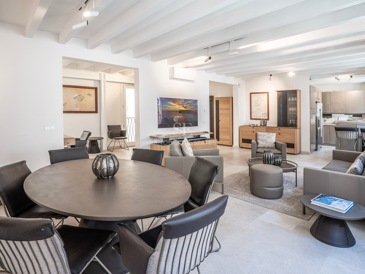 Modern living room with round dining table, leather sofas, white beamed ceiling, and wall-mounted TV.