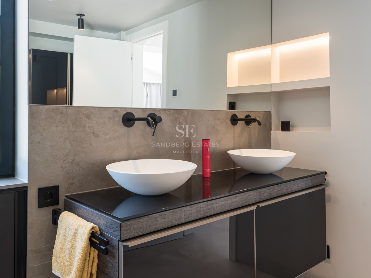 Contemporary bathroom featuring two white vessel sinks on a dark vanity with matte black wall-mounted faucets and mood lighting.