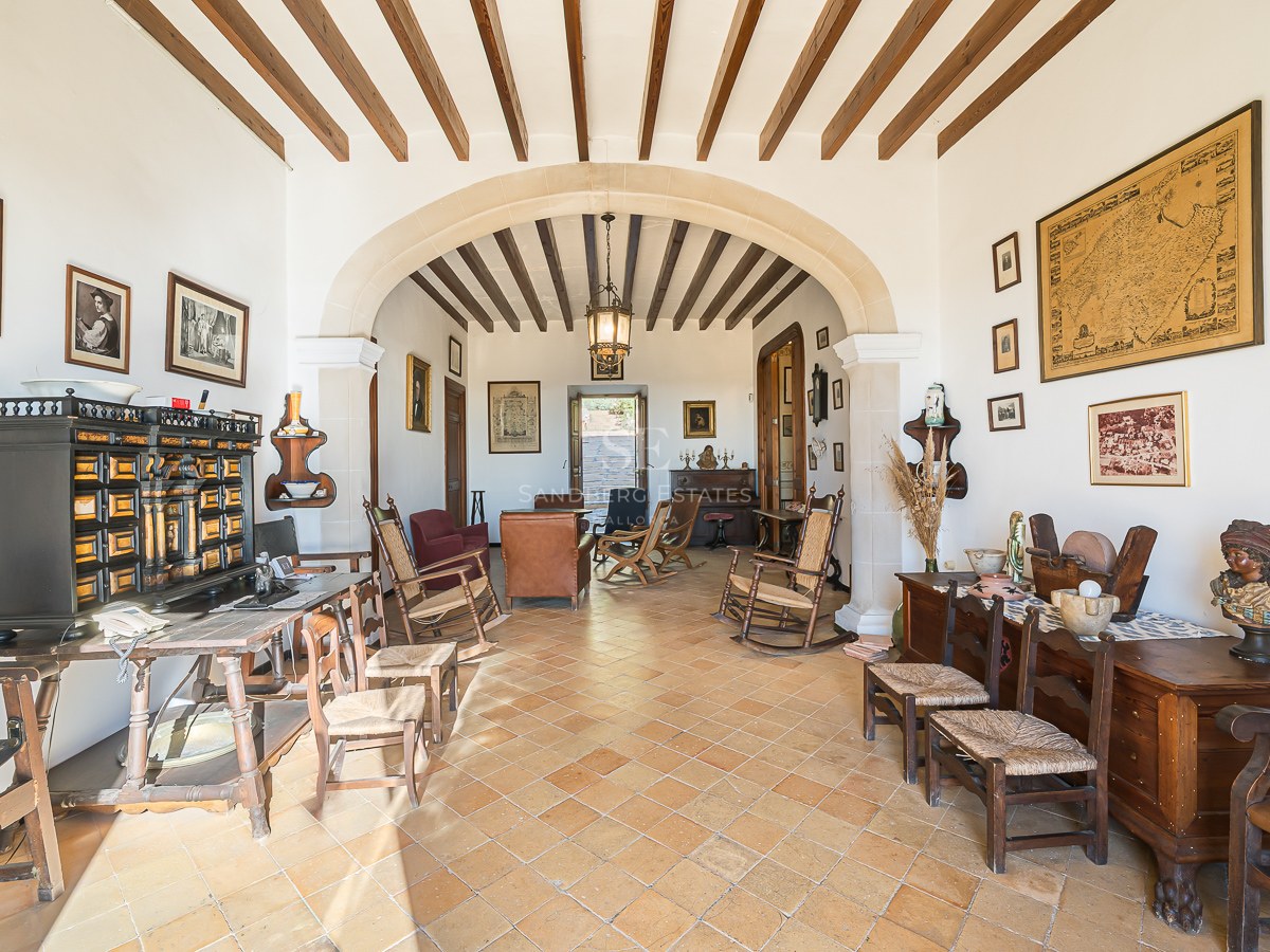 Amplio salón con suelos de terracota, vigas de madera vistas, un gran arco de piedra y mobiliario rústico antiguo.