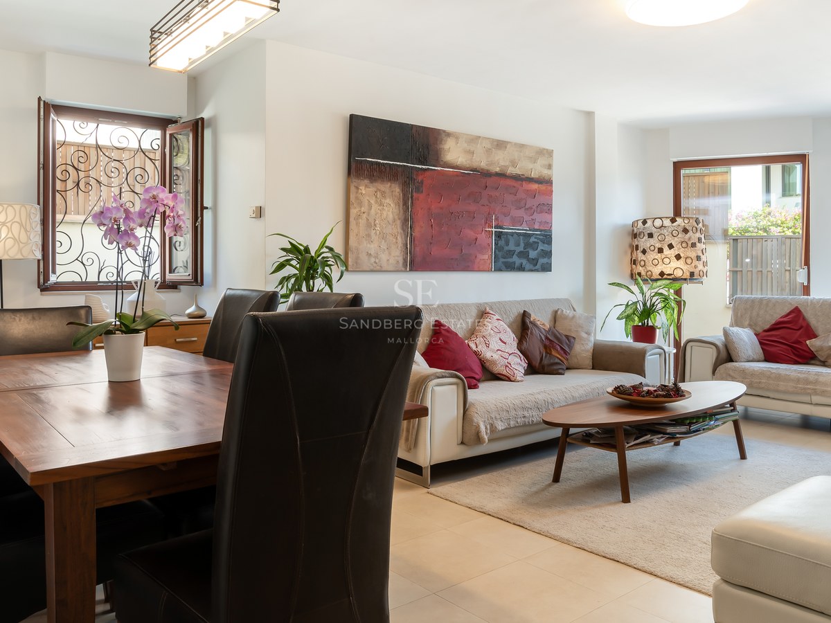 Salón comedor de planta abierta con sofás beige, mesa de madera, sillas de cuero negro y ventanas con rejas decorativas.