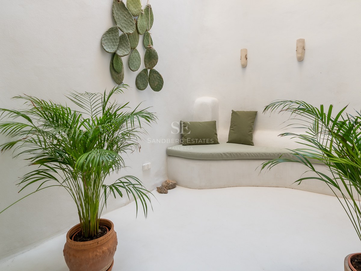 Salon minimaliste blanc avec banquette intégrée incurvée, coussins vert sauge et plantes d'intérieur.