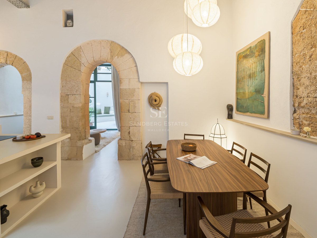 Salle à manger contemporaine avec table en bois sous des suspensions globes, encadrée par des arches en pierre.