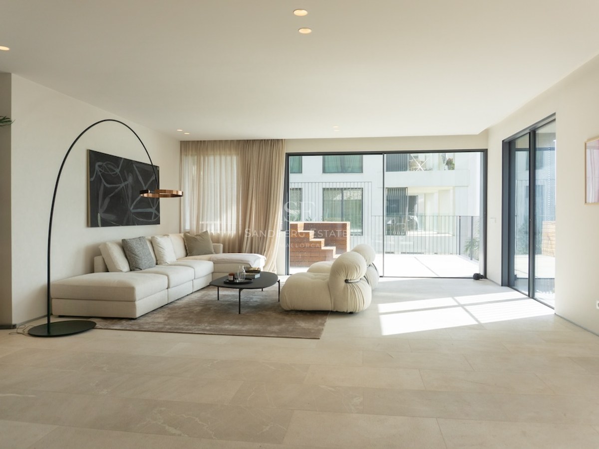 Ljust minimalistiskt vardagsrum med beige stengolv, off-white hörnsoffa och stora skjutdörrar i glas.