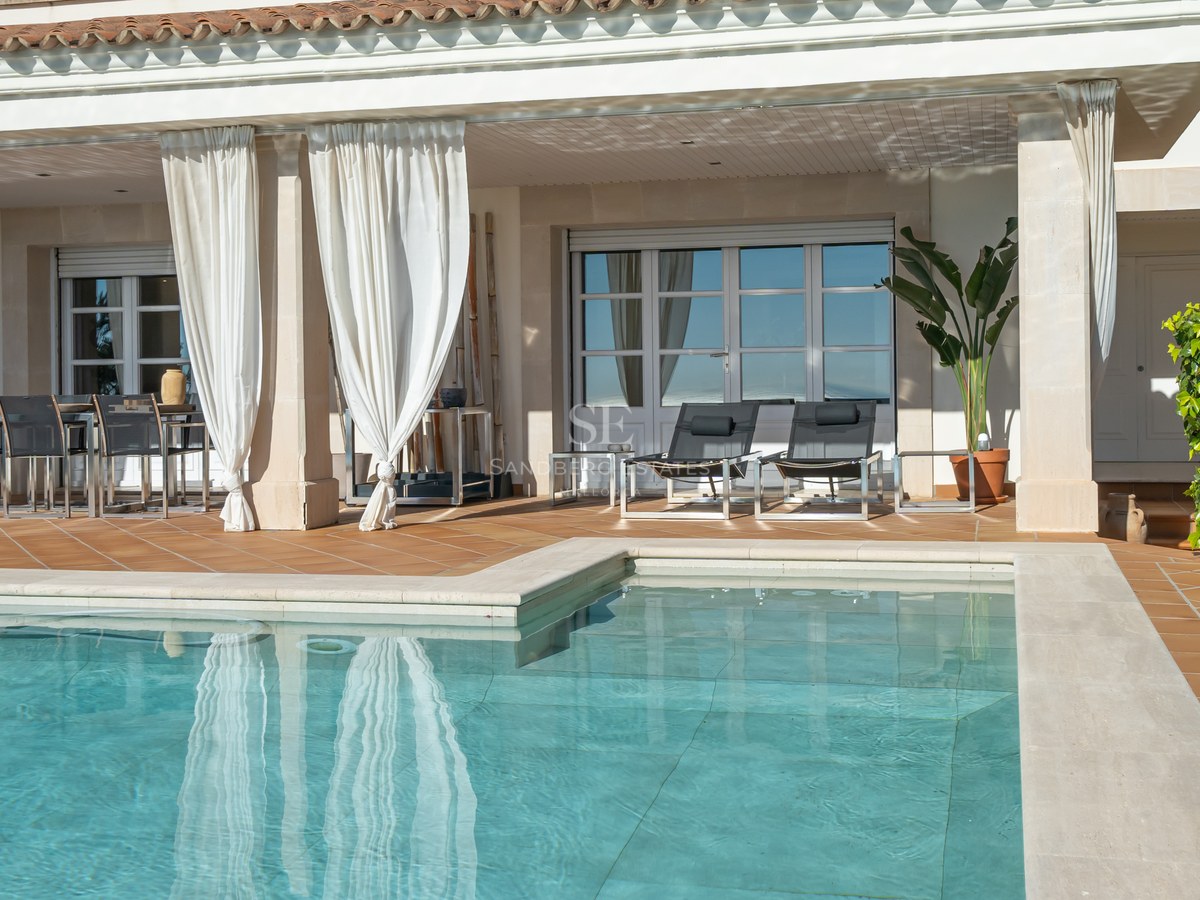 Terrasse en terre cuite avec piscine, rideaux blancs, chaises longues et coin repas extérieur abrité.
