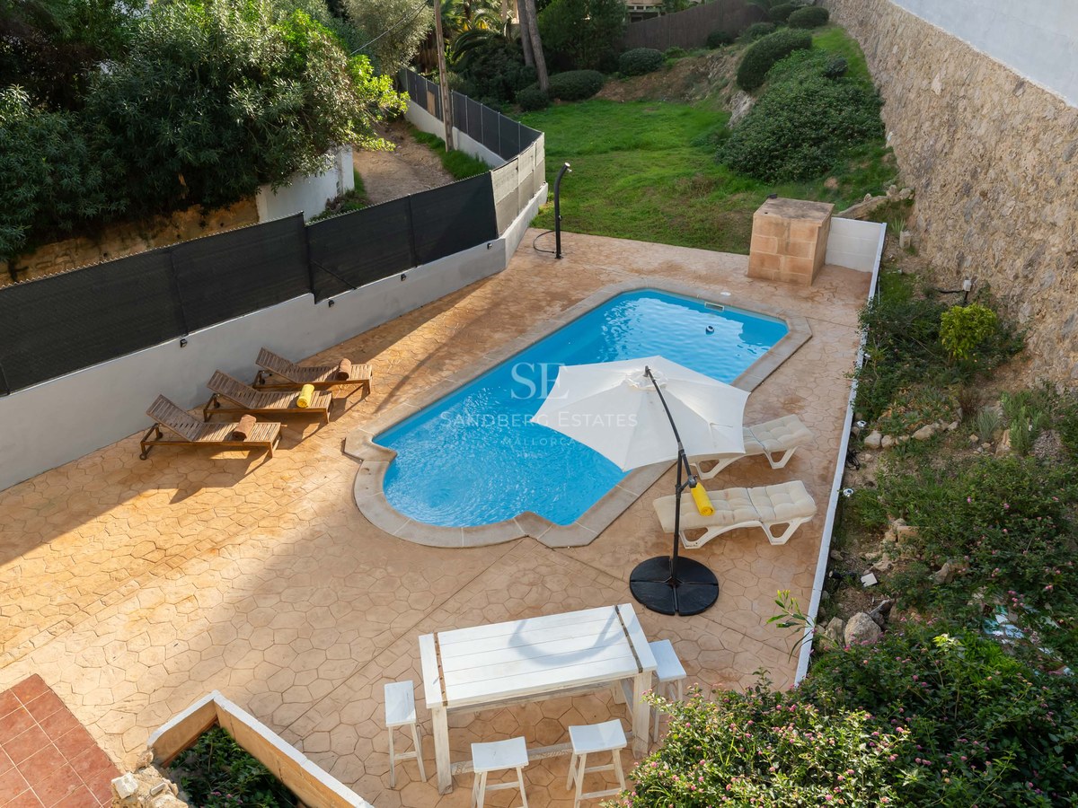 Overhead view of a turquoise swimming pool surrounded by a terracotta patio, sun loungers, and an outdoor dining area.