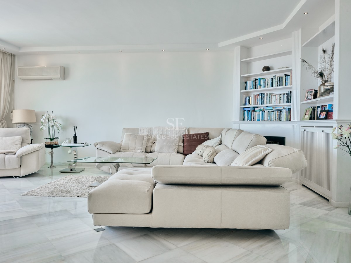 Spacious living room featuring a large beige sectional sofa, polished marble flooring, and built-in white bookshelves.
