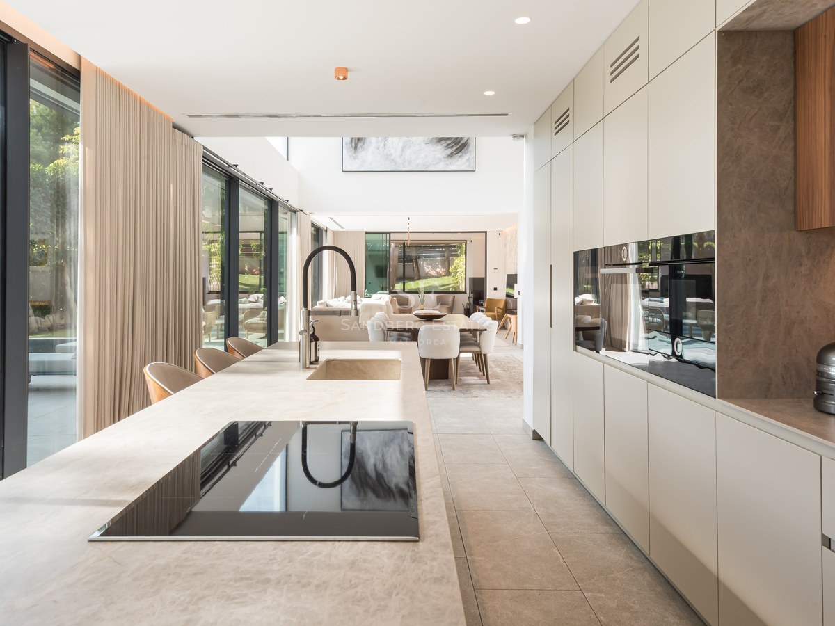 Cuisine moderne avec un grand îlot en pierre, des appareils intégrés et des baies vitrées donnant sur une piscine.