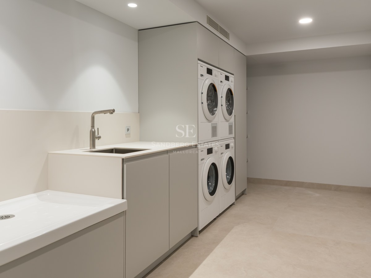 Buanderie moderne équipée de lave-linge et sèche-linge Miele, rangements épurés et grand bac de lavage.