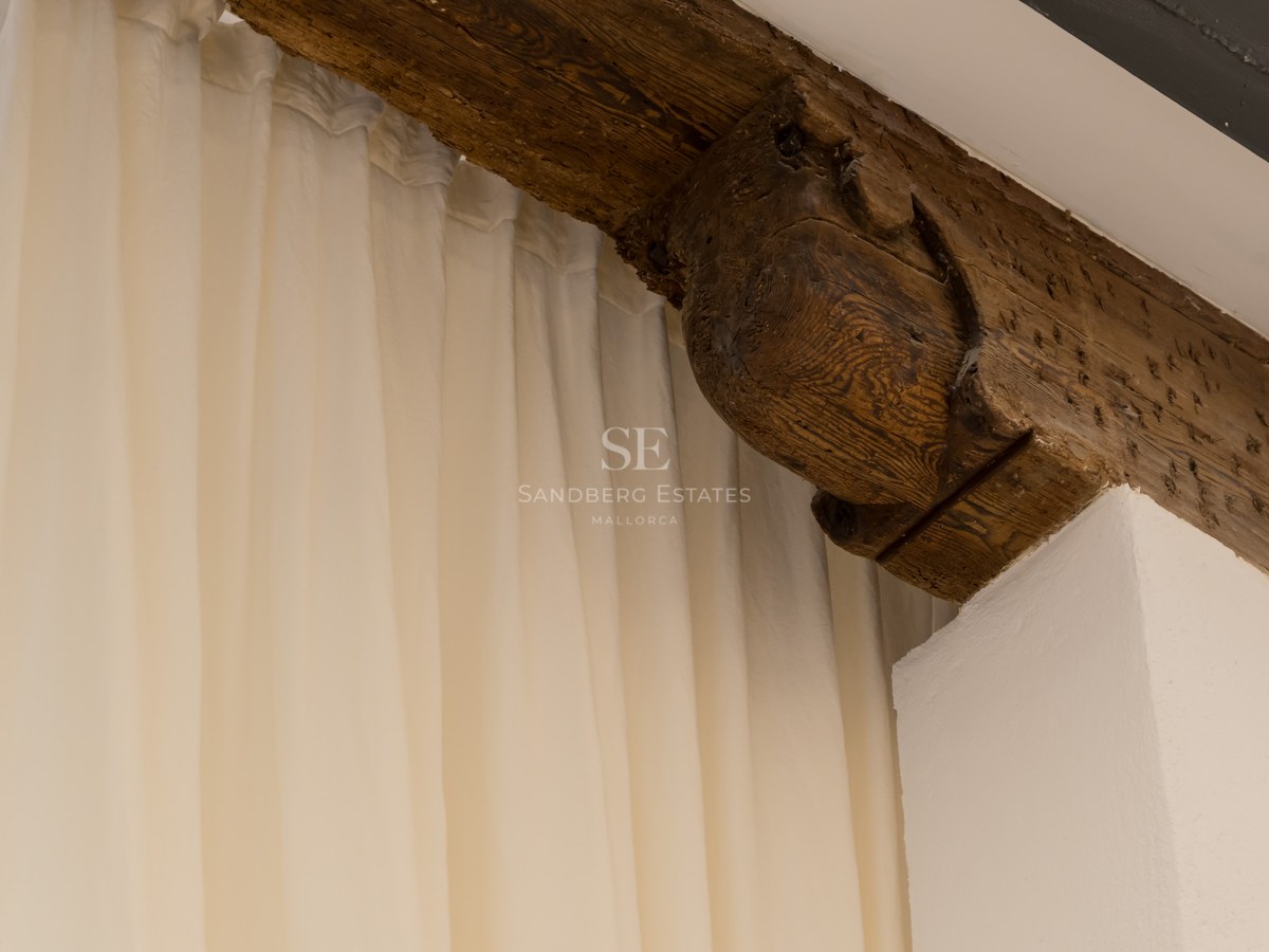 Poutre en bois sombre sculptée à la main à côté de rideaux crème et mur blanc.