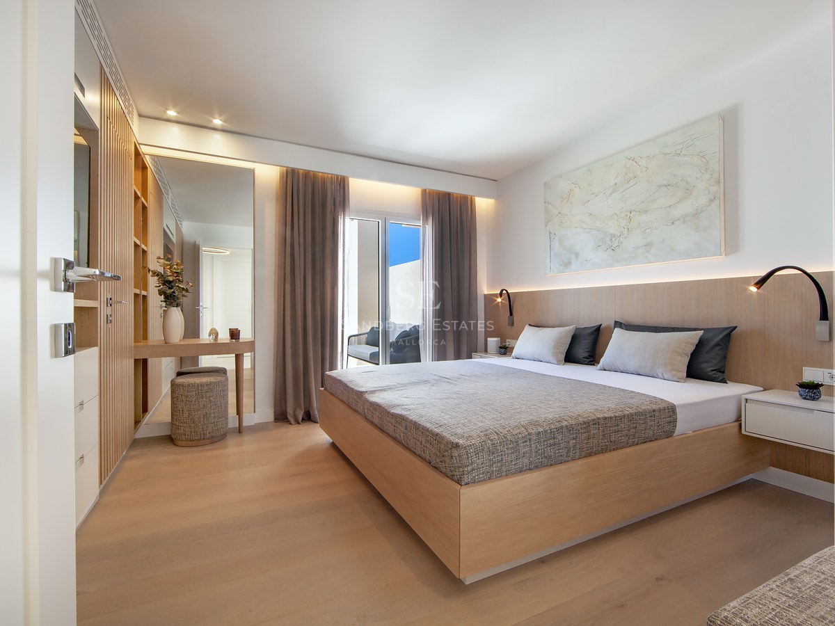Modern master bedroom with a large wooden bed, integrated lighting, wood paneling, and access to a sunny balcony.
