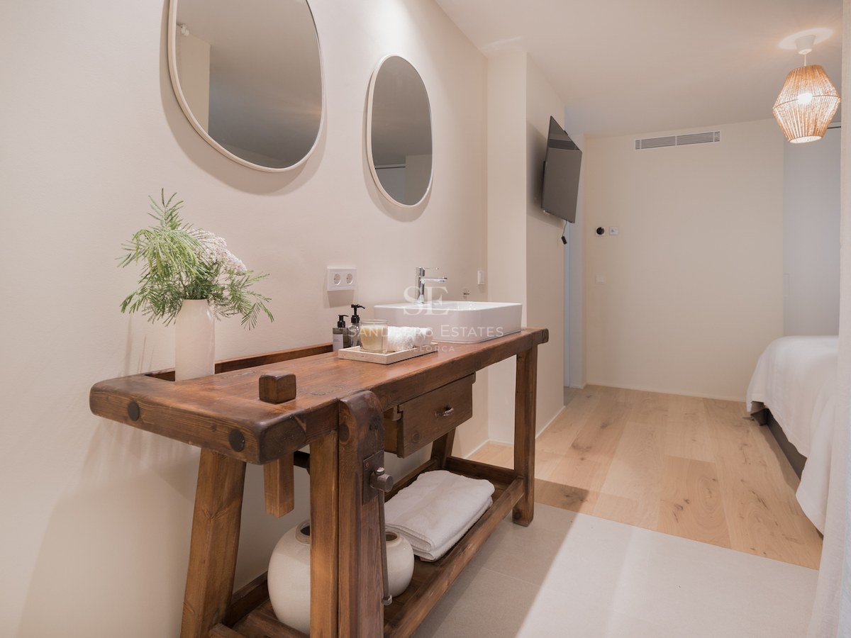 Salle de bain avec meuble en bois massif, vasque blanche et deux miroirs ovales sur mur blanc cassé.
