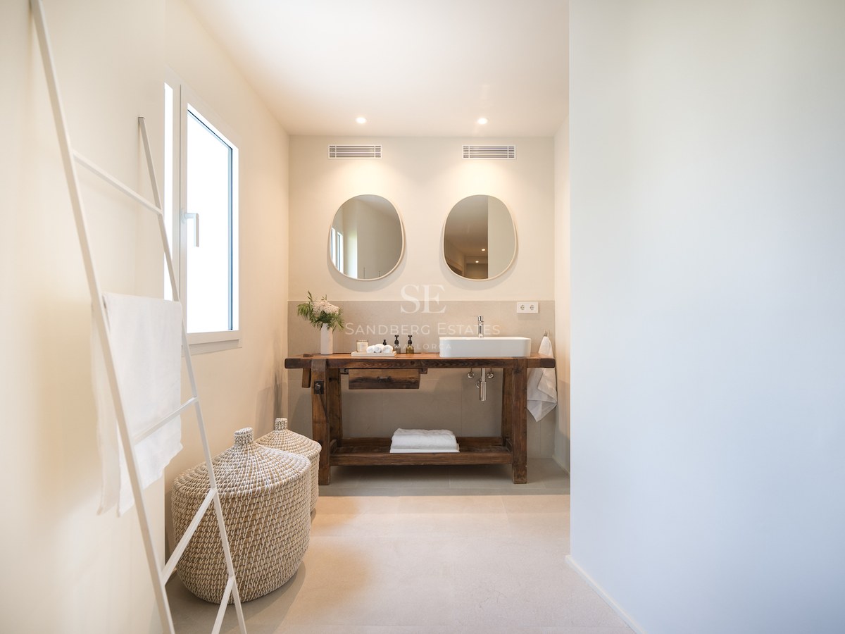 Salle de bains moderne avec meuble en bois de récupération, vasque à poser, miroirs organiques et paniers en osier.