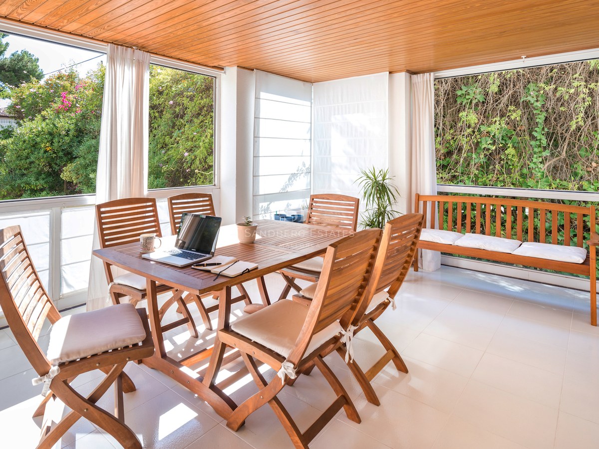 Une terrasse ensoleillée avec table à manger en bois, chaises et banc, donnant sur la verdure du jardin.