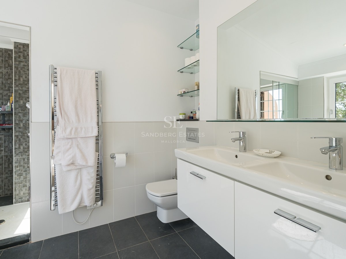 Salle de bain moderne avec double vasque blanche, grand miroir, sèche-serviettes et douche à l'italienne.