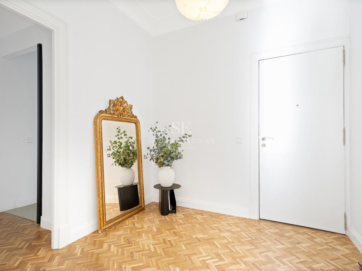 Bright foyer with white walls, herringbone wood floors, a large gold mirror, and a white door.