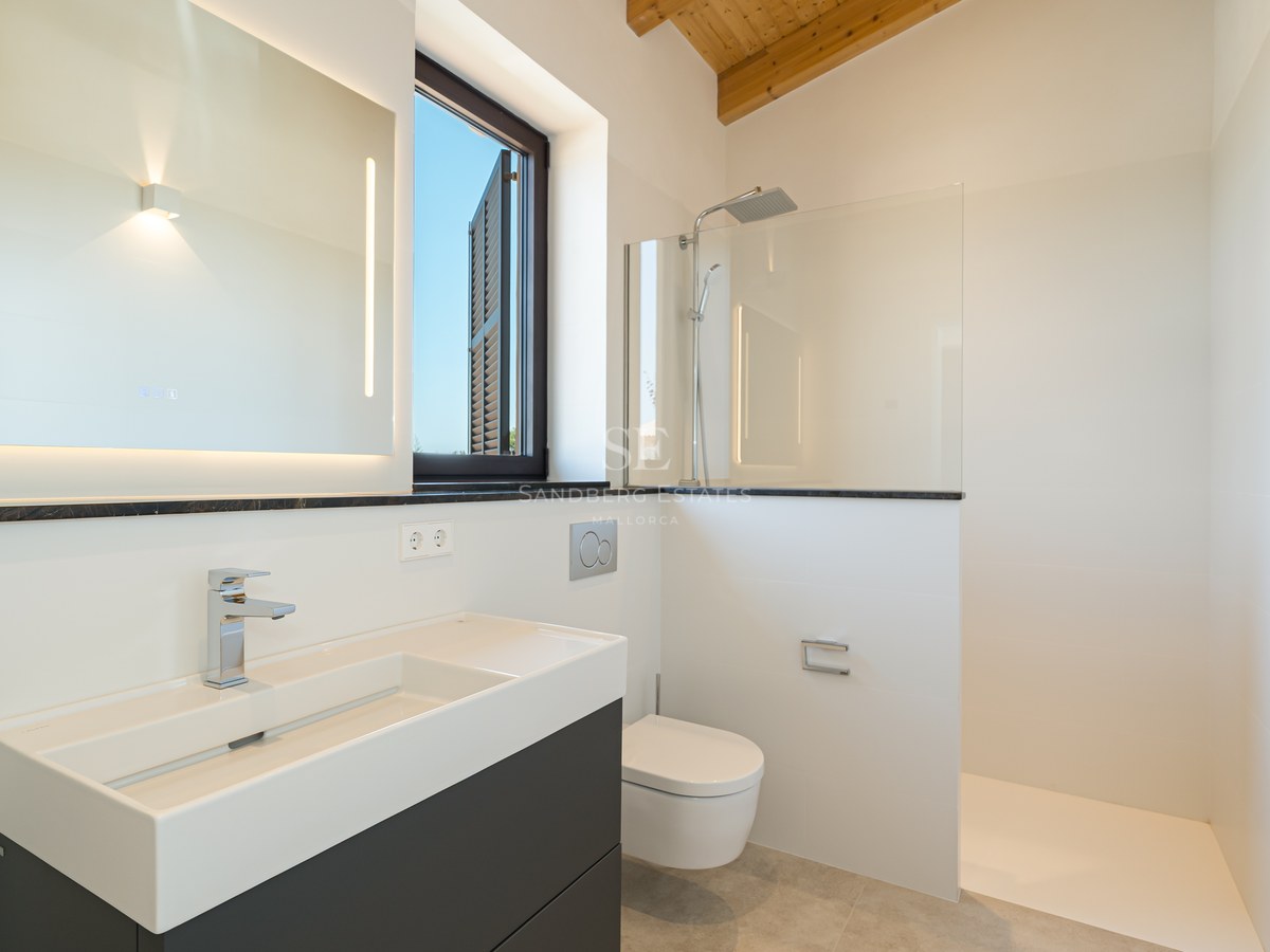 Modern white bathroom with walk-in shower, floating vanity, LED mirror, and natural wood ceiling beams.