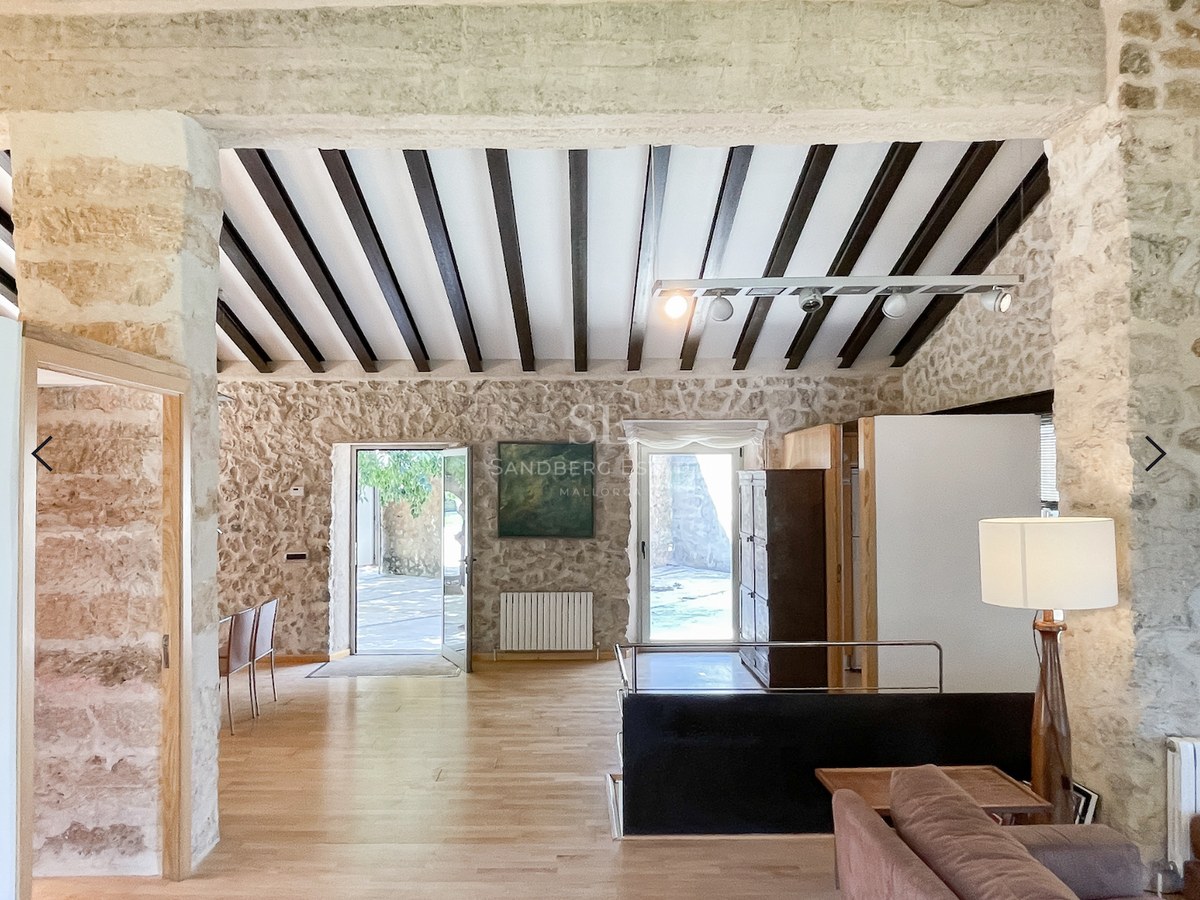 Salón de planta abierta con paredes de piedra natural, vigas oscuras en el techo y suelos de roble claro.