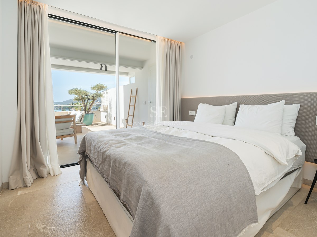 Chambre lumineuse avec grand lit, sol en pierre et baies vitrées ouvrant sur une terrasse ensoleillée.
