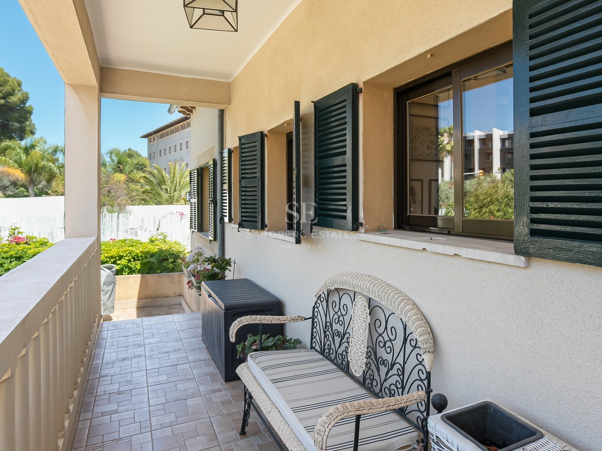 Covered balcony featuring a wrought iron bench, green Mallorcan shutters, and views of lush greenery.