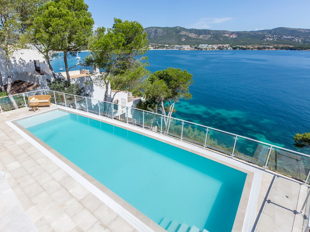 An elevated view of a turquoise infinity pool overlooking the Mediterranean sea with mountains in the background.