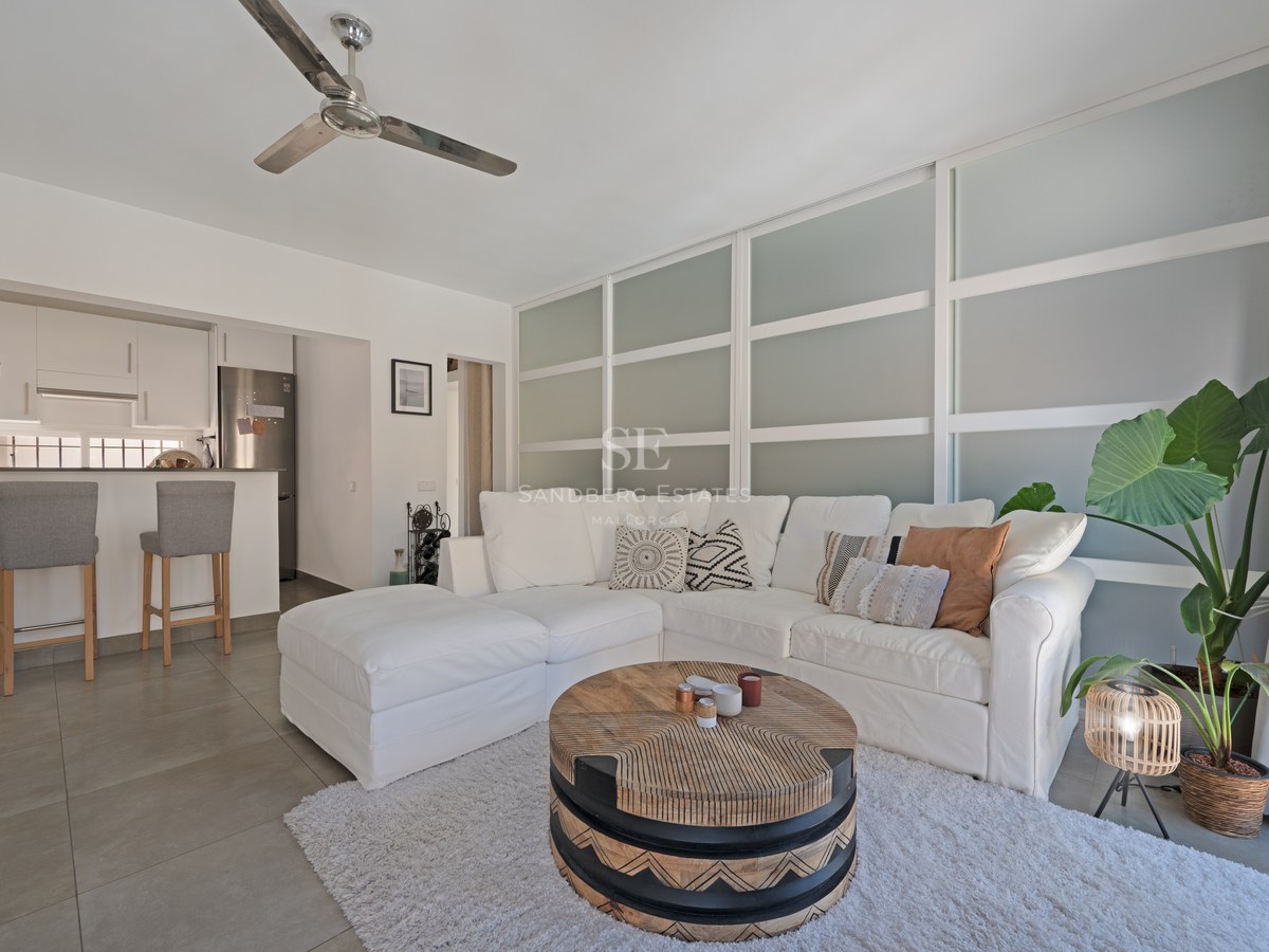 Modern living room with white corner sofa, round wooden coffee table, and an open kitchen with breakfast bar.