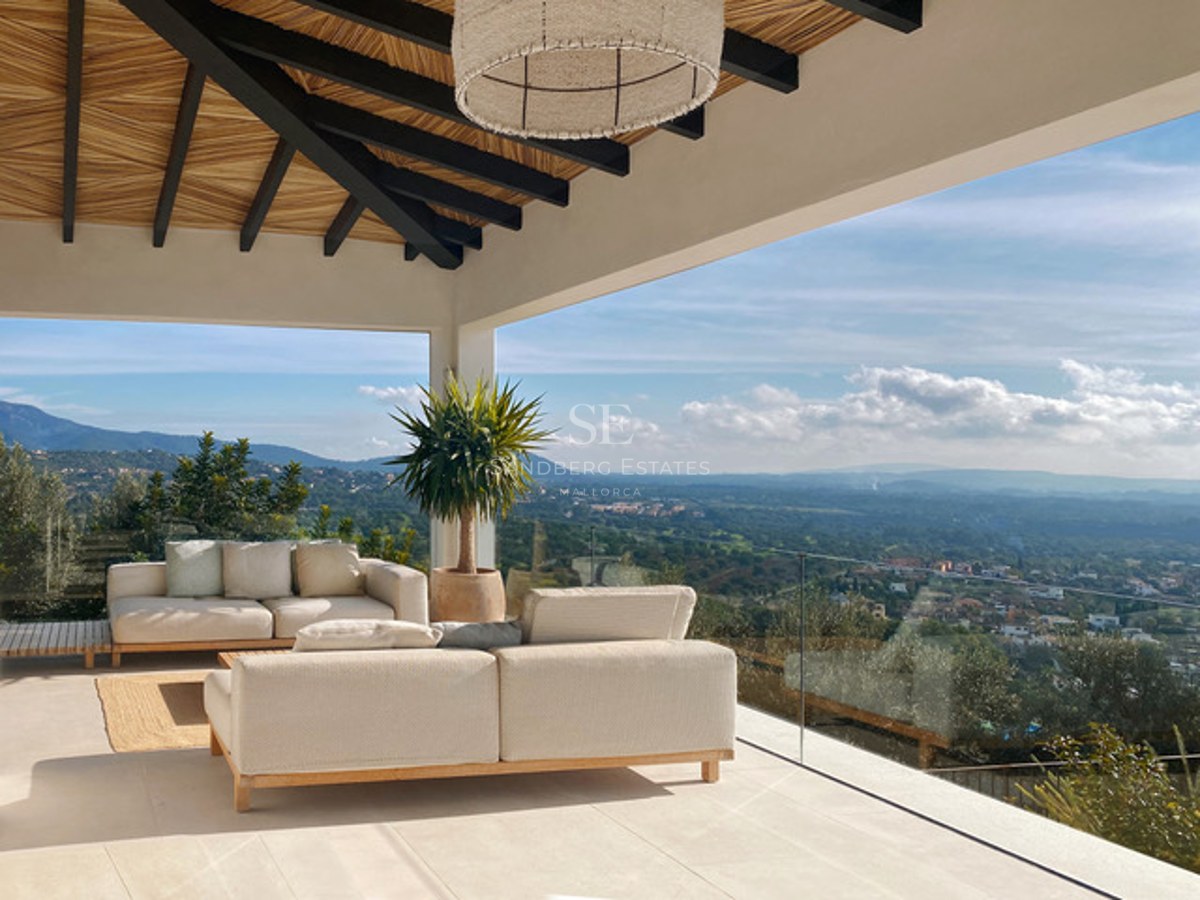 Terrasse moderne avec canapés crème, plafond en bois et garde-corps en verre offrant une vue sur la vallée.