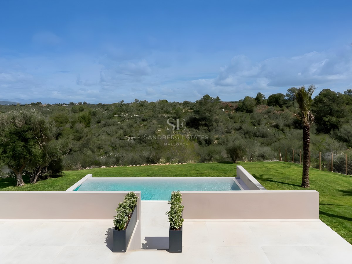 Elevated view of a rectangular infinity pool with light stone terrace overlooking green Mediterranean hills.