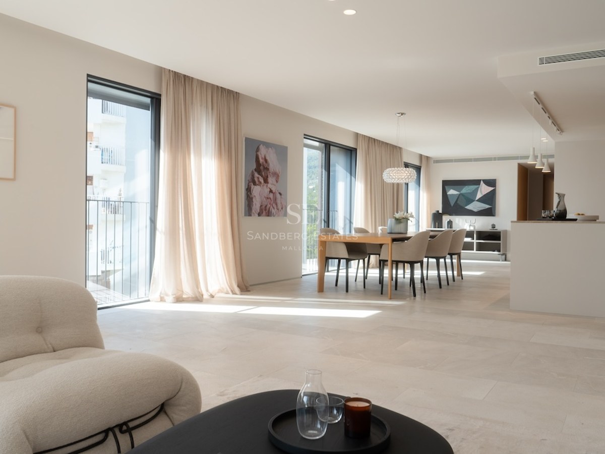 Ljust vardagsrum med öppen planlösning, naturstensgolv, stora fönsterpartier och moderna möbler.