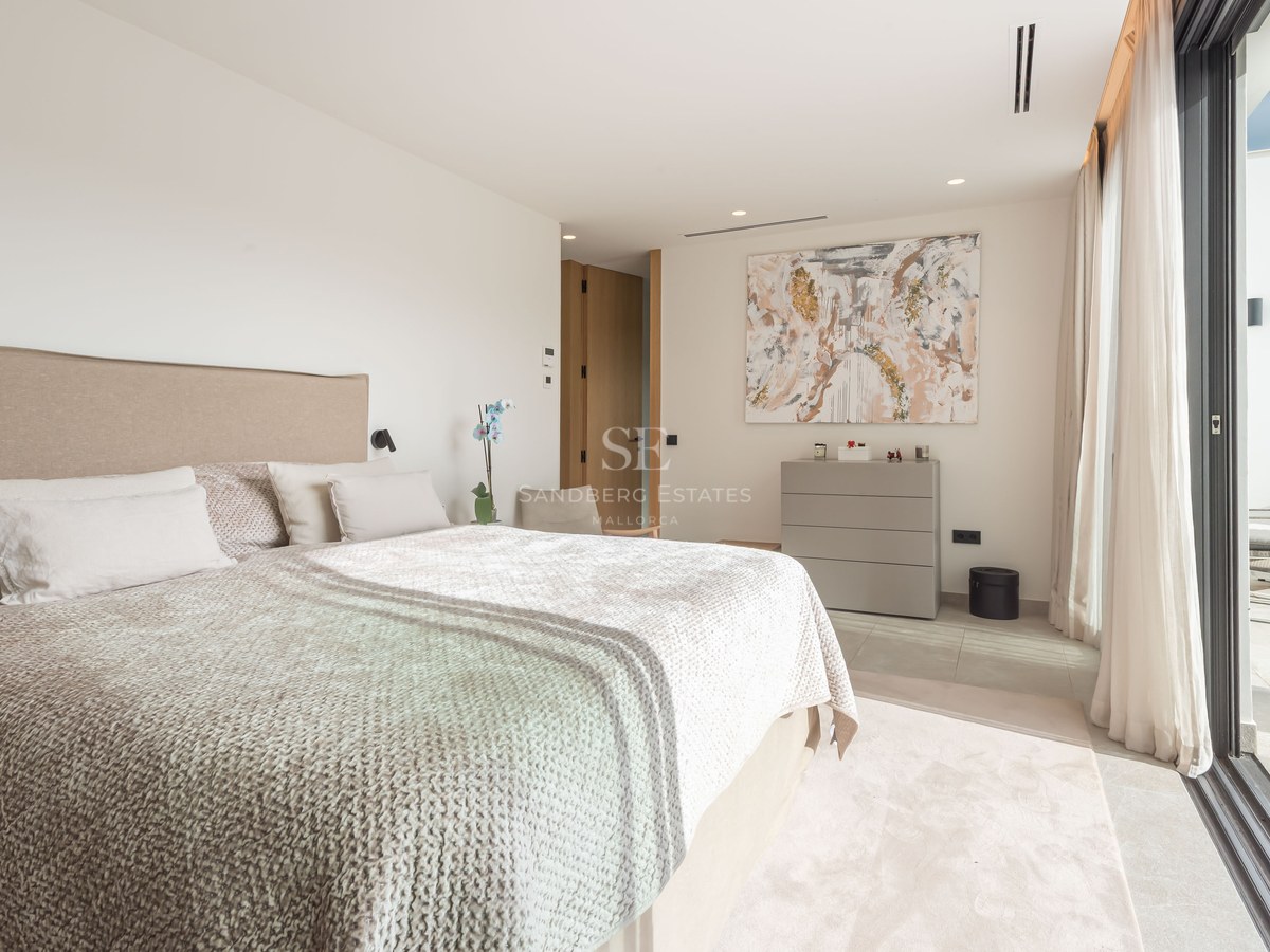 Chambre principale lumineuse avec un grand lit, art abstrait et baies vitrées coulissantes ouvrant sur une terrasse.