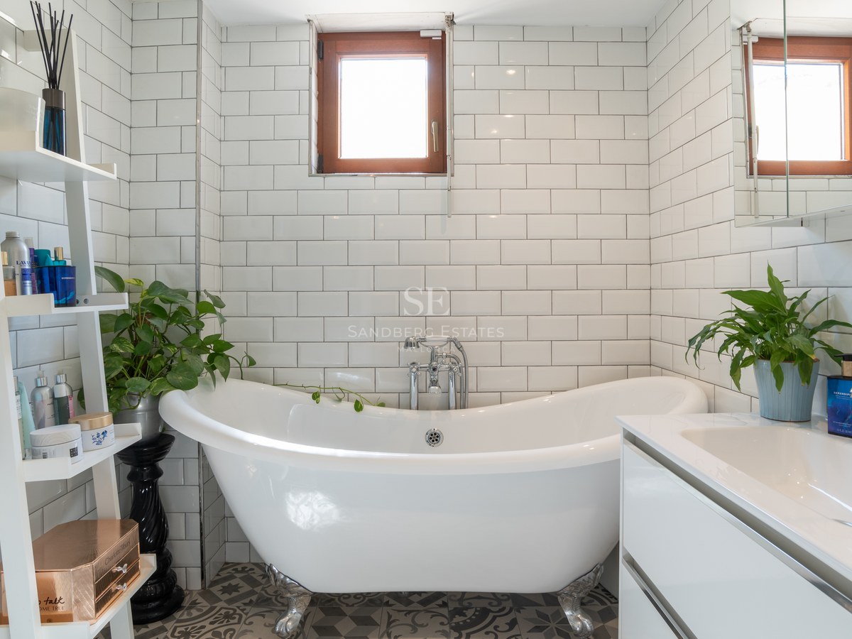 Baño luminoso con bañera exenta de patas, azulejos tipo metro y mueble de lavabo moderno blanco.