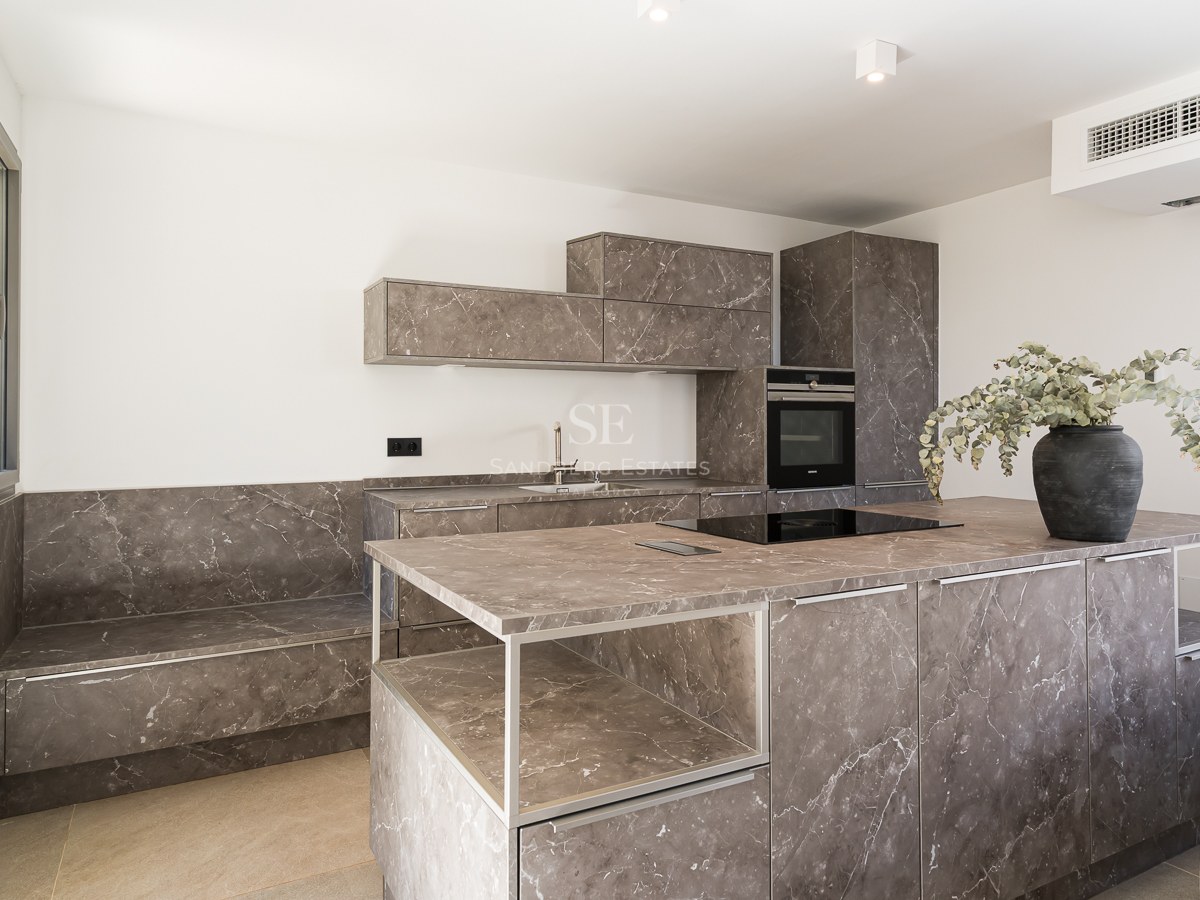 Moderne Küche mit großer Insel in grau gemasertem Stein, integrierten Geräten und minimalistischen weißen Wänden.