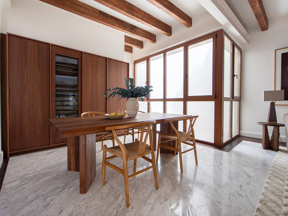 Modern dining room featuring marble floors, wood ceiling beams, a large wooden table, and integrated wine cellar.