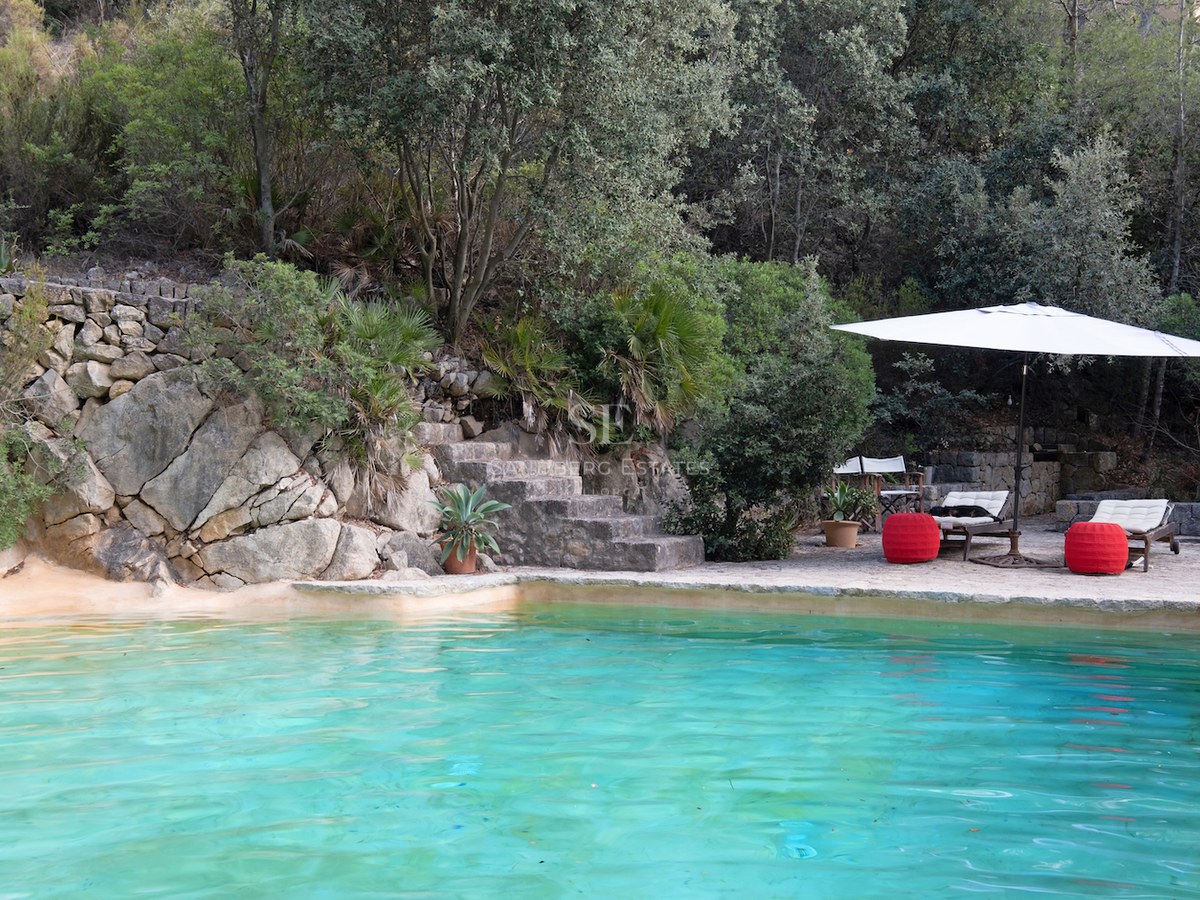 Piscine aux eaux turquoise nichée contre une paroi rocheuse naturelle avec des escaliers en pierre et une végétation dense.