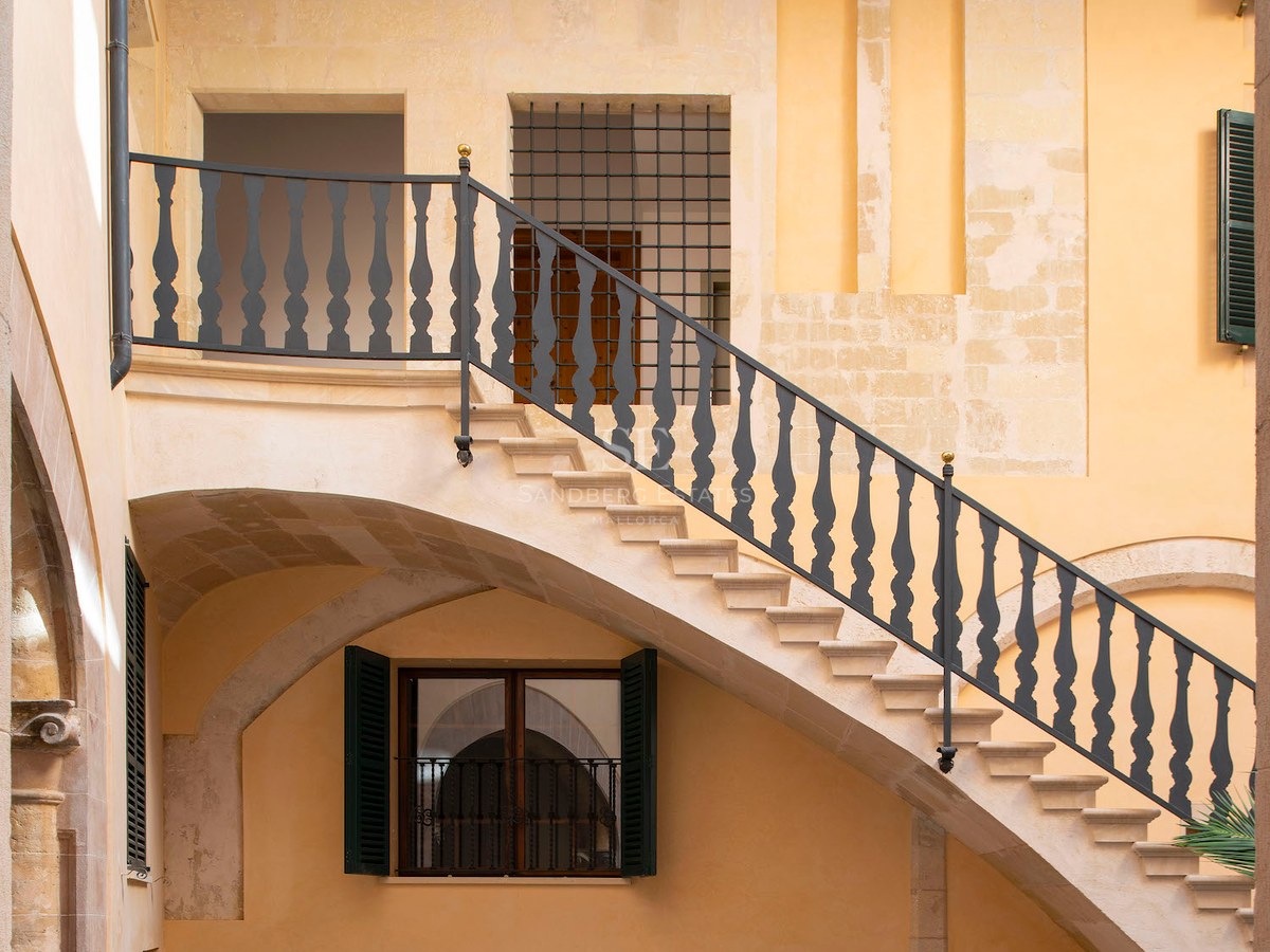 View of an inner courtyard with a stone staircase, black wrought iron railings, and warm ochre stone walls.