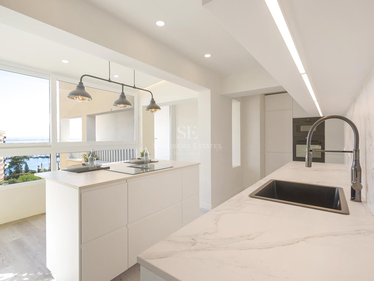 Cuisine moderne lumineuse avec îlot blanc, plans de travail en marbre et fenêtre donnant sur un port de plaisance.