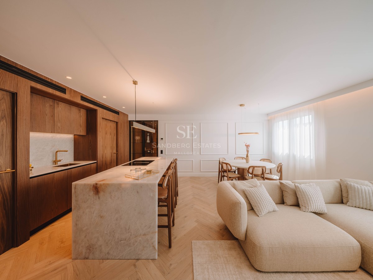 Espace moderne ouvert avec îlot en marbre, armoires en bois, parquet en chevrons et grand canapé beige.