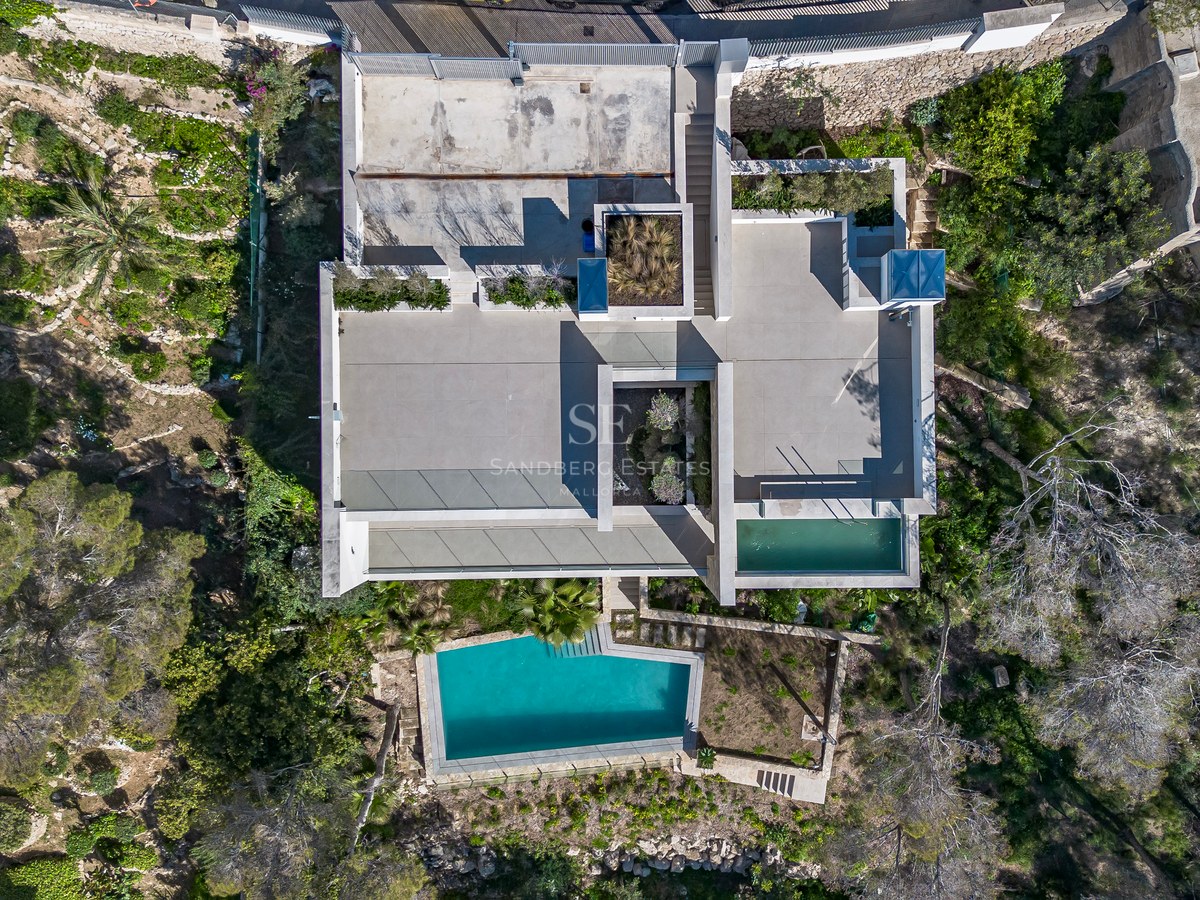 Vue aérienne d'une villa moderne géométrique avec toits plats, terrasses et piscine turquoise cristalline.
