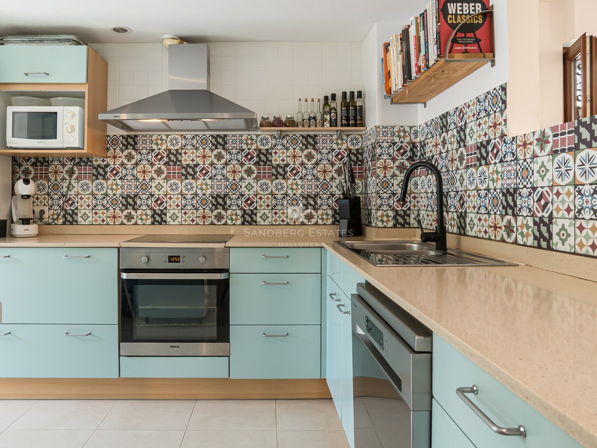 Cocina con muebles verde menta, encimera beige y azulejos decorativos de estilo hidráulico.
