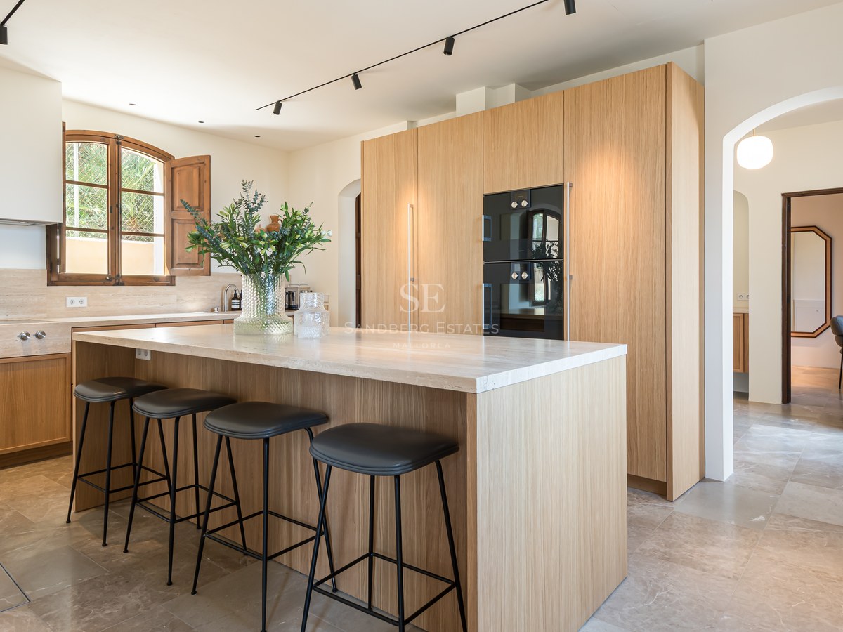 Cuisine contemporaine avec meubles en chêne, îlot en pierre naturelle, tabourets noirs et sol en marbre.